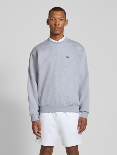 Männermodel trägt Regular Fit Sweatshirt aus Baumwoll-Mix von Lacoste in hellgrau mit glatter Struktur, Ganzkörperansicht von vorne. Herren Sweatshirt