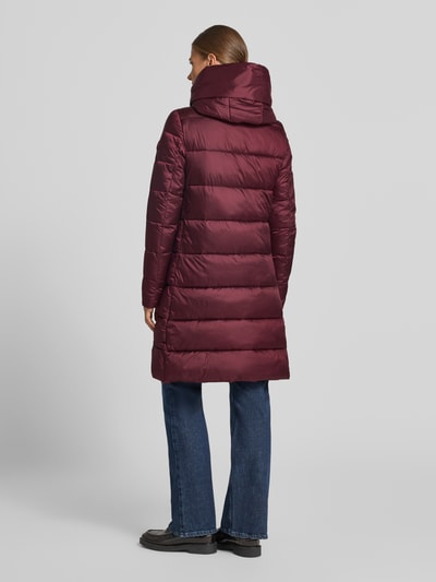 Frauenmodel trägt Steppmantel mit Kapuze Modell 'LYSA' von Save The Duck in Dunkelrot, glatte Textur, gerader Schnitt, Ganzkörperansicht Rückansicht.