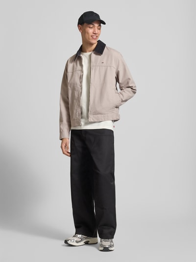 Męski model nosi Regular Fit Ranch-Jacke aus reiner Baumwolle von Tommy Jeans, jednokolorowa kurtka, zamek błyskawiczny, wyhaftowane logo, wykładany kołnierz ze sztruksu, regulacja szerokości, boczne kieszenie, bawełna, Ganzkörperansicht von vorne.