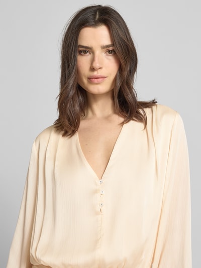 Frauenmodel trägt Minikleid mit kurzer Knopfleiste Modell 'MAGALI' von Guess in Creme mit V-Ausschnitt und Volantsaum, Nahaufnahme Oberkörper. Damen Minikleid, Taillierter Schnitt, seitlicher Knopf- und Reißverschluss, Rückenlänge 88 cm, Brustweite 46 cm, Ärmellänge 72 cm.