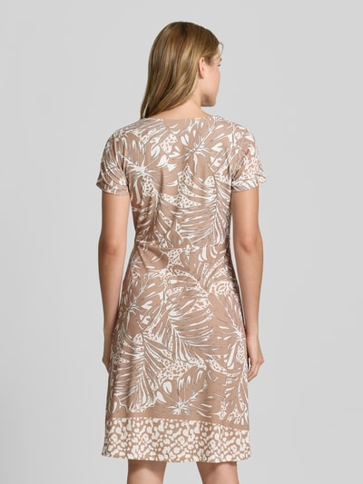 Frauenmodel trägt Knielanges Kleid in Wickel-Optik von More & More mit Allover-Muster in Beige und Weiß, Material-Mix mit Stretch, Ganzkörperansicht Rückansicht.