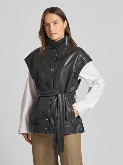 Frauenmodel trägt Regular Fit Weste mit Viskose-Anteil Modell 'JACARO' von BOSS Orange in Schwarz, Kunstleder, Stehkragen, Gürtelschlaufen, seitliche Eingrifftaschen, Ganzkörperansicht von vorne