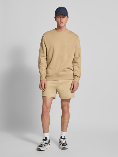 Männermodel trägt Regular Fit Shorts aus katoenmix van Tommy Jeans in effen kleuren met logodetail en tunnelkoord, sweat materiaal, steekzakken, achterzak, boord, ganzkörperansicht van voren.
