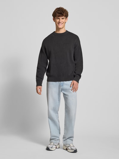 Männermodel trägt Oversized Strickpullover mit Logo und Rundhalsausschnitt von Pegador in Schwarz, reine Baumwolle, Ganzkörperansicht von vorne.