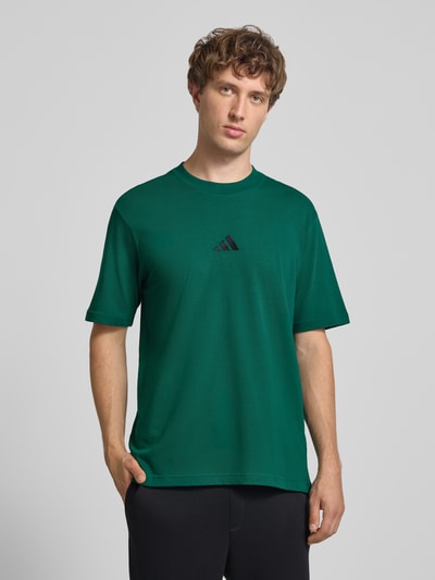 Männermodel trägt Regular Fit T-Shirt aus reiner Baumwolle von adidas Sportswear in donkergroen, logo op de borst, Ganzkörperansicht von vorne.
