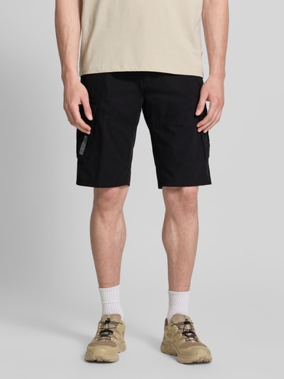Männermodel trägt Relaxed Fit Cargoshorts aus reiner Baumwolle von s.Oliver BLACK LABEL, unifarben schwarz, seitliche Cargotaschen, Ganzkörperansicht von vorne.