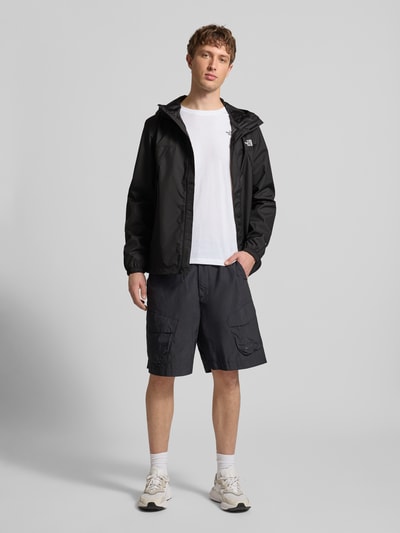 Męski model nosi kurtkę z logo model 'ANTORA' od The North Face, krój regular fit, czarna, z kapturem i zamkiem błyskawicznym, długość tyłu 74 cm, szerokość ramion 46 cm, szerokość w rozmiarze M 58 cm, długość rękawów 69 cm, pełny widok z przodu.