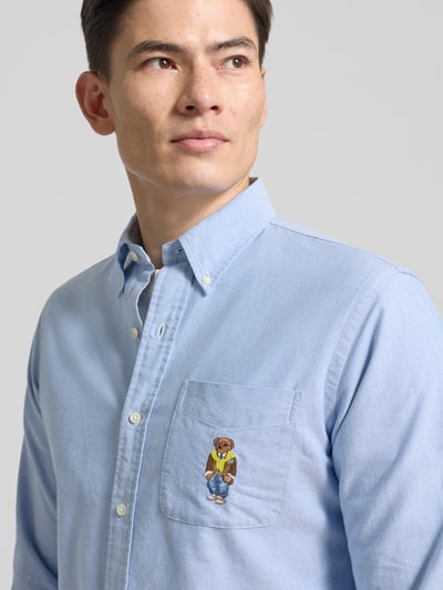 Mannenmodel draagt Custom Fit Freizeithemd mit Motiv-Stitching van Polo Ralph Lauren in lichtblauw katoen met borstzak en button-down kraag, nahaufnahme bovenlichaam.