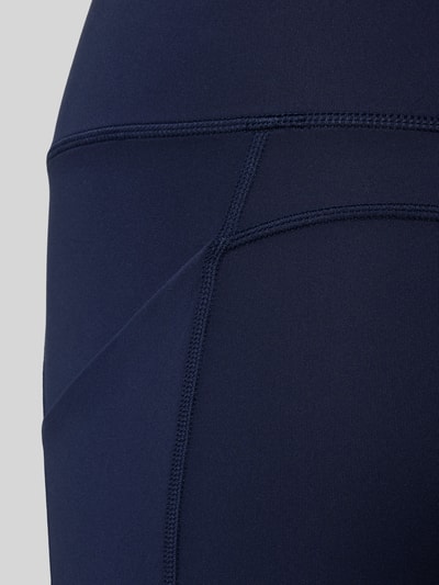 Frauenmodel trägt Flared Fit Leggins mit breitem Bund Modell 'OASIS' von Fabletics, dunkelblauer Elastikstoff, Detailaufnahme.