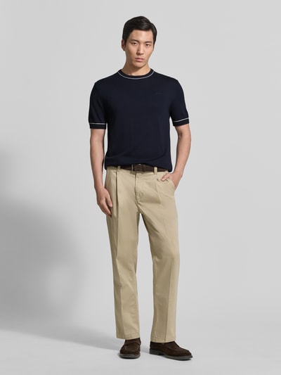 Männermodel trägt Strickshirt mit Rundhalsausschnitt von Gant in Dunkelblau, gerader Schnitt, Kurzarm, kombiniert mit heller Stoffhose, Ganzkörperansicht von vorne.