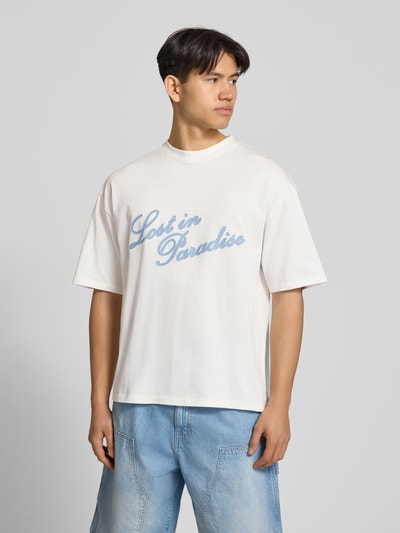 Männermodel trägt T-Shirt mit Logo- und Statement-Stitching von REVIEW aus reiner Baumwolle, gerader Schnitt, helle Farben, Ganzkörperansicht von vorne.