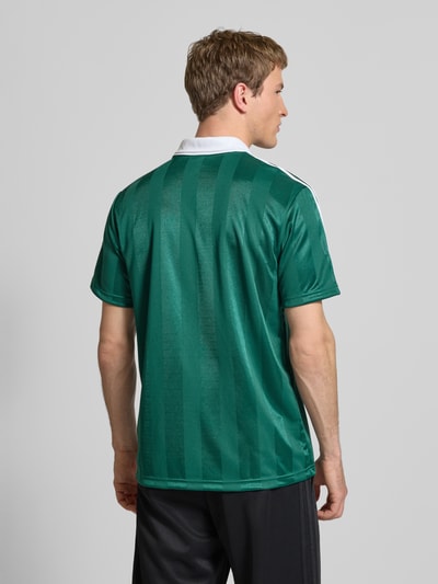Männermodel trägt Trikot mit Umlegekragen und Label-Print von adidas Originals in Grün mit weißen Details, Regular Fit, Rückenlänge 73 cm, Ganzkörperansicht Rückansicht.