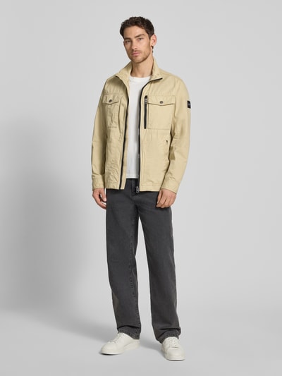 Męski model nosi Regular Fit Jacke aus reiner Baumwolle von Tom Tailor, dwukolorowy, krój regular fit, zamek błyskawiczny, wpuszczane kieszenie zapinane na zamek błyskawiczny, nakładane brustasza, kieszeń wewnętrzna, beżowe odcienie, gładka faktura, ganzkörperansicht z przodu.