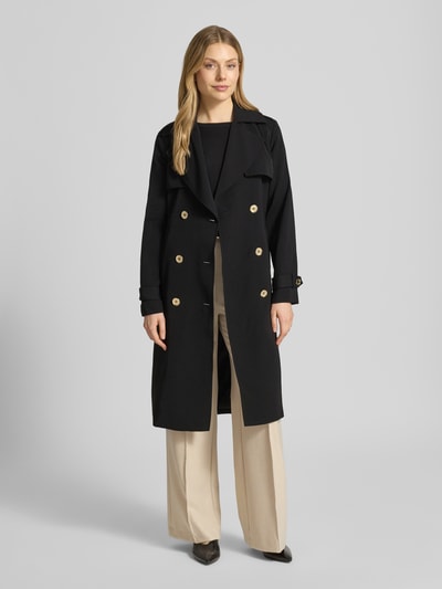 Modelka kobieca ma na sobie dwurzędowy trencz z wiązanym paskiem MICHAEL Michael Kors, czarny, krój regular fit; przód całej sylwetki. Długość tyłu w rozmiarze S: 47 cm, szerokość ramion w rozmiarze S: 40 cm, szerokość klatki piersiowej w rozmiarze S: 50 cm, długość rękawów w rozmiarze S: 63 cm.