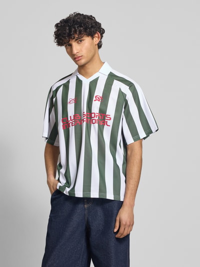 Männermodel trägt Loose Fit Poloshirt mit Motiv-Print Modell 'ZIDAN' von Only & Sons, grün-weiß gestreiftes Piqué, Ganzkörperansicht von vorne.
