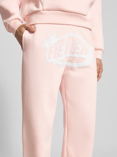 Frauenmodel trägt Straight Leg Sweatpants mit Logo und elastischem Bund von Review in zartem Rosa, Baumwoll-Mix, Nahaufnahme Oberkörper.
