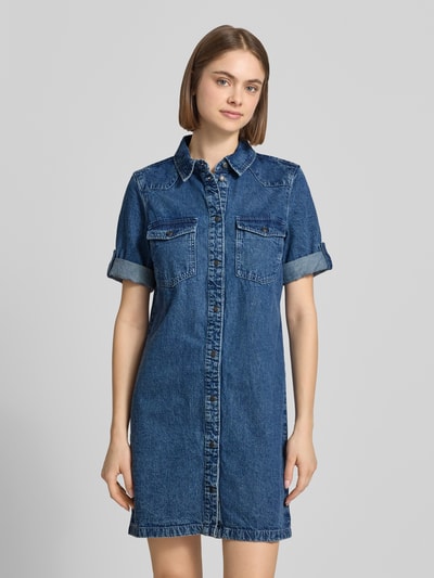 Frauenmodel trägt Jeanskleid mit Brusttaschen Modell 'NEW SIGNE' von Noisy May, Reine Baumwolle, Gerader-Schnitt, Minikleid, Hemdblusenkragen, Ärmel mit Aufschlag, Rückenlänge Größe S 87 cm, Brustweite 49 cm, Ärmellänge 24 cm, kräftiges Denimblau, strukturierte Oberfläche, Ganzkörperansicht von vorne.