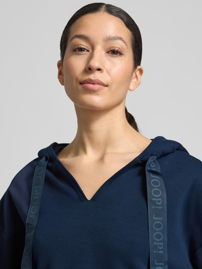 Frauenmodel trägt Oversized Hoodie aus Baumwoll-Mix Modell 'Tristani' von JOOP! in Dunkelblau mit Kapuze und V-Ausschnitt, Nahaufnahme Oberkörper.