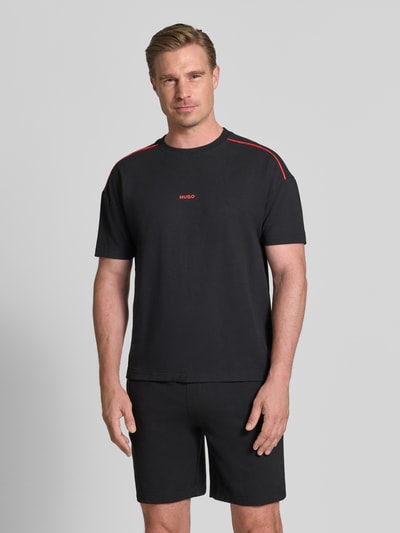 Männermodel trägt Regular Fit T-Shirt aus Baumwoll-Mix Modell 'NOAH' von HUGO in Schwarz mit roten Details, Ganzkörperansicht von vorne. Herren T-Shirt von HUGO