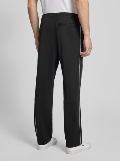 Männermodel trägt schwarze Regular Fit Sweatpants mit Baumwoll-Anteil von Lacoste, seitliche Galonstreifen, Rückansicht Ganzkörperansicht.