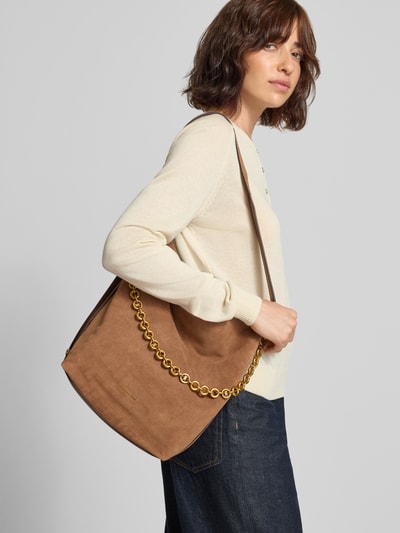 Frauenmodel trägt Handtasche aus Leder mit Label-Applikation Modell 'NOLITA' von MICHAEL Michael Kors in Braun mit goldener Kette, Nahaufnahme Oberkörper. Echtes Leder, Magnetverschluss, Schulterriemen, Maße 35x33x17 cm, Riemenlänge 72 cm.