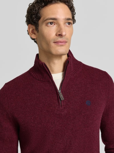 Männermodel trägt Regular Fit Strickpullover aus reiner Wolle von MCNEAL in Bordeaux mit Logo-Stickerei, Nahaufnahme Oberkörper. Rückenlänge 65 cm, Ärmellänge 50 cm, Troyer-Kragen, gerippte Bündchen.
