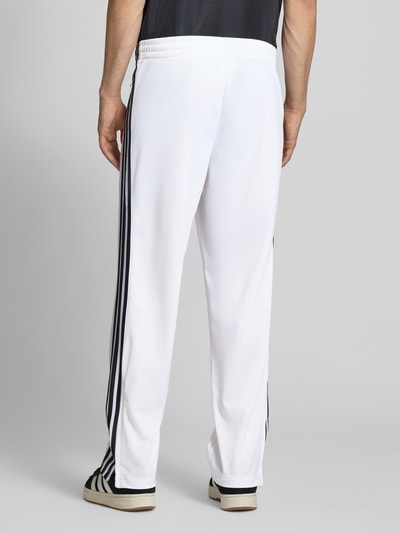 Männermodel trägt Regular Fit Sweatpants mit Label Print van adidas Originals met all-over motief, regular fit, labelprint, elastische boord, zij-steekzakken, heren sweatpants, ganzkörperansicht rückansicht.