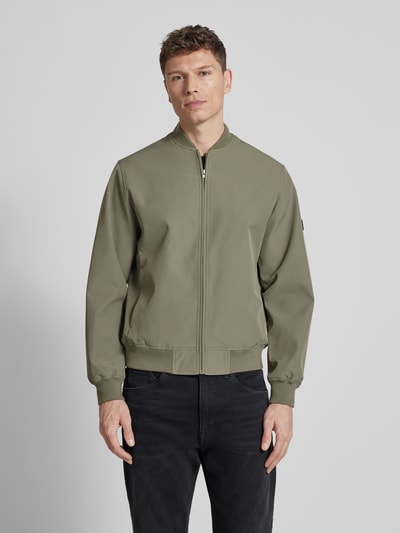 Männermodel trägt olivgrüne Bomberjacke mit Stehkragen Modell 'BLAASPEN' von Jack & Jones Premium, lockerer Schnitt, Ganzkörperansicht von vorne.