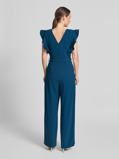 Frauenmodel trägt Jumpsuit mit Rüschen und Bindegürtel von Apricot in Blau, Material-Mix mit Stretch, Ganzkörperansicht Rückansicht.