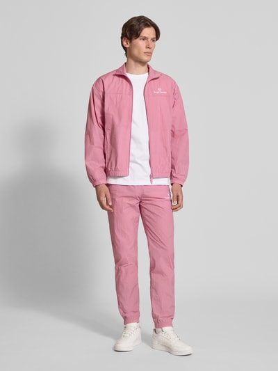 Männermodel trägt Straight Fit Stoffhose mit Logo-Stitching Modell 'Nayla' von SERGIO TACCHINI in Rosa, elastischer Bund mit Tunnelzug, elastische Beinabschlüsse, Innenbeinlänge bei Größe M 77 cm, Ganzkörperansicht von vorne.