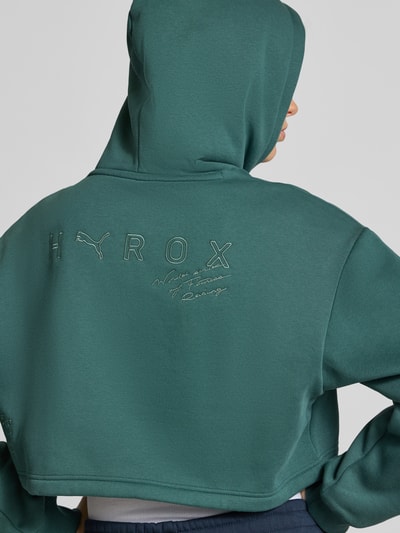 Frauenmodel trägt Regular Fit Sweatshirt aus Baumwoll-Mix PUMA X HYROX von PUMA in Dunkelgrün, Damen Sweatshirt, Ganzkörperansicht Rückansicht.
