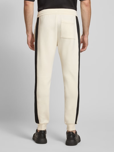 Männermodel trägt Sweatpants mit Bordüre von Armani Exchange in Creme mit schwarzer Label-Print-Bordüre, Ganzkörperansicht Rückansicht.