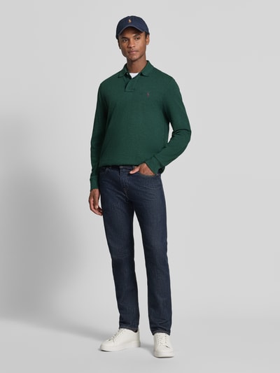 Męski model nosi Regular Fit Poloshirt aus reiner Baumwolle von Polo Ralph Lauren, zielona koszulka polo, ciemnoniebieskie dżinsy, białe sneakersy, czapka z daszkiem, gładkie tekstury, widok całej sylwetki z przodu, kontekst: koszulka polo męska Polo Ralph Lauren.