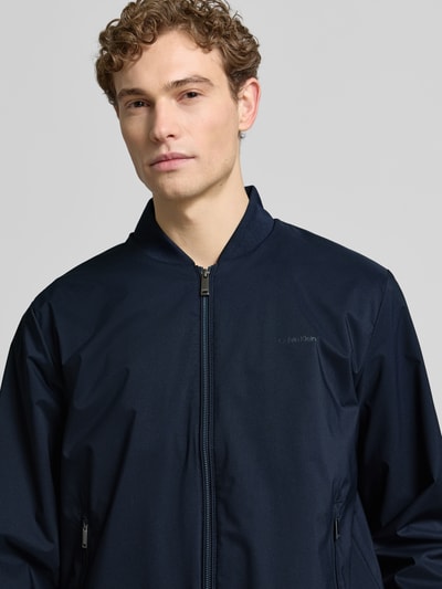 Männermodel trägt Bomberjacke mit Reißverschlusstaschen Modell 'MATTE' von CK Calvin Klein in Dunkelblau, Nahaufnahme Oberkörper.