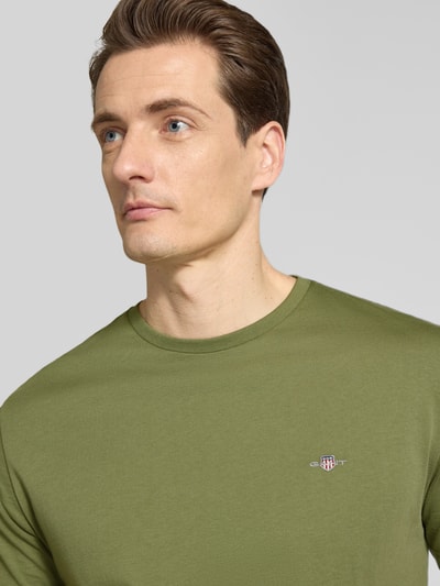 Männermodel trägt Regular Fit T-Shirt mit Logo-Stitching von Gant aus reiner Baumwolle in Olivgrün, Nahaufnahme Oberkörper.
