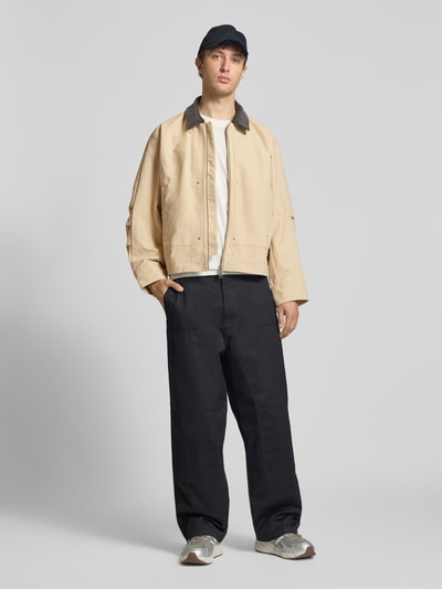 Männermodel trägt Regular Fit Jeansjacke aus reiner Baumwolle von adidas Originals in Beige, mit Umlegekragen, Logo-Detail, Zweiwege-Reißverschluss, unifarbene Optik, Denim-Textur, Ganzkörperansicht von vorne.