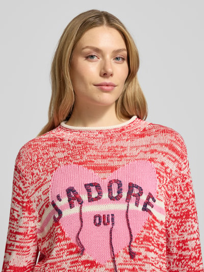 Kobiece modelka nosi Sweter z dzianiny z prążkowanymi wykończeniami od Oui z bawełny, luźny krój, detal z logo, okrągły dekolt, zbliżenie na górę ciała.