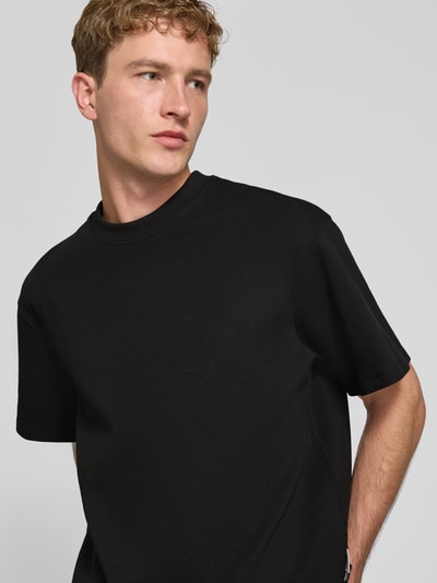 Männermodel trägt schwarzes Relaxed Fit T-Shirt aus elastischem Baumwoll-Mix Modell 'SCUBA' von JACK & JONES, Nahaufnahme Oberkörper. Rückenlänge bei Größe M: 68 cm, Rundhalsausschnitt.