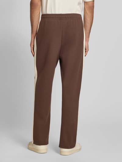 Männermodel trägt Straight Fit Sweatpants mit Logo-Stitching von KARL KANI in Braun mit Elastischer-Material-Mix, Ziernähte, Ganzkörperansicht Rückansicht.