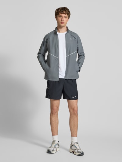 Männermodel trägt Regular Fit Jacke mit Stehkragen Modell 'Miler' von NIKE TRAINING in Grau, Logo-Print, Reißverschluss, Ganzkörperansicht von vorne. Rückenlänge 67 cm, Ärmellänge 64 cm, Größe M.