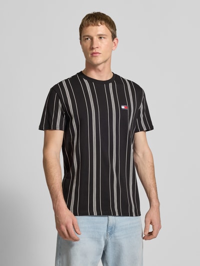 Männermodel trägt Regular Fit T-Shirt aus reiner Baumwolle von Tommy Jeans mit Optik: Allover-Muster, Label-Stitching-Applikation, Kurzarm, Rundhals, Ganzkörperansicht von vorne.