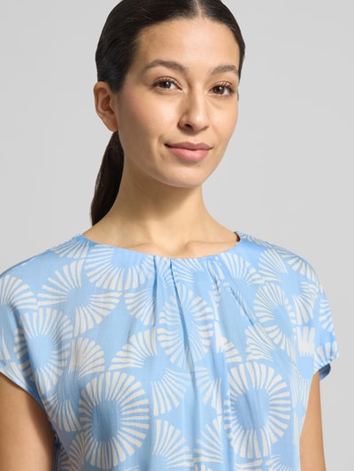 Frauenmodel trägt Blusenshirt aus Viskose mit Rundhalsausschnitt von More & More, hellblau mit weißem Allover-Muster, Nahaufnahme Oberkörper.