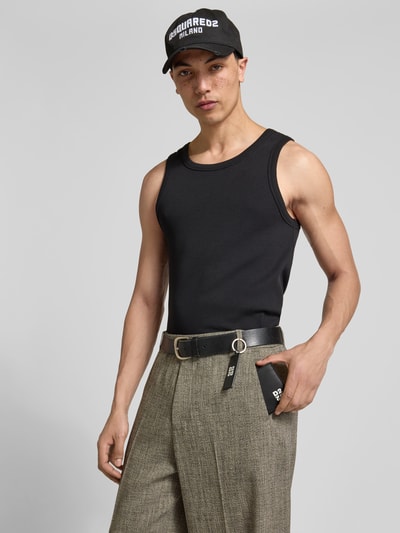 Mannelijk model draagt zwart shirt, grijze broek met riem, houdt Portemonnaie met Logo-Prägung van Dsquared2, Nahaufnahme Oberkörper.