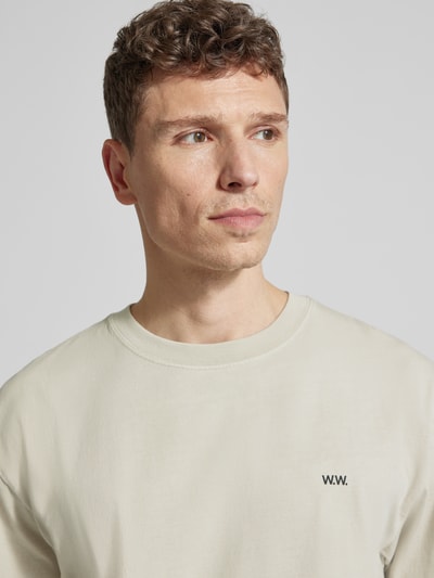 Męski model nosi T-Shirt mit Logo-Print Modell 'Gary' od Wood Wood z bawełny, jasny kolor, gładka tekstura, z bliska, górna część ciała