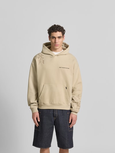 Männermodel trägt Oversized Hoodie aus Baumwoll-Mix von Don’t Waste Culture in Beige mit Florale-Stickereien, Känguru-Tasche, elastische Abschlüsse, Rückenlänge bei Größe M: 70 cm, Ganzkörperansicht von vorne.