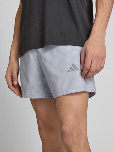 Mężczyznamodel nosi Regular Fit Shorts mit Logo-Allover-Muster model 'WE BRLO SHO' von adidas Training, efekt: jednolity kolor, wykończenie materiału: satyna, wzór z logo na całej powierzchni, detal z logo, elastyczny ściągacz, boczna kieszeń zapinana na zamek błyskawiczny, krój regular fit, Ganzkörperansicht z przodu