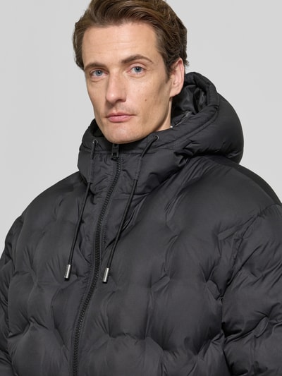 Männermodel trägt Regular Fit Steppjacke mit Rumpftunnelzug Modell 'Barbo2641' von HUGO, Popeline-Struktur, schwarze Farbe, Nahaufnahme Oberkörper.