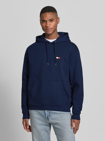 Männermodel trägt Regular Fit Hoodie aus reiner Baumwolle von Tommy Hilfiger, Optik: Unifarben dunkelblau, Logo-Applikation, Kängurutasche, Kapuze mit Tunnelzug, Langarm, Ärmelabschluss und Rumpfabschluss gerippt, Materialverarbeitung: Sweat, Ganzkörperansicht von vorne.