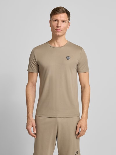 Männermodel trägt T-Shirt aus Viskose-Mix mit Label-Patch von EA7 Emporio Armani, Slim-Fit, beige, Rundhalsausschnitt, Ganzkörperansicht von vorne.