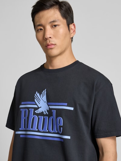 Männermodel trägt Regular Fit T-Shirt aus reiner Baumwolle von RHUDE, Schwarz mit blauem Label-Print, Rundhalsausschnitt, Nahaufnahme Oberkörper.